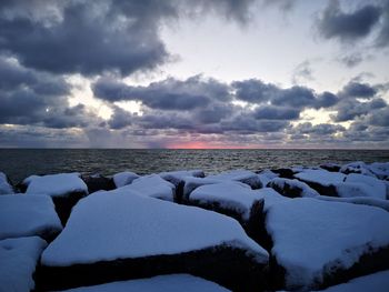 Snow covered land and sea against sky during sunset