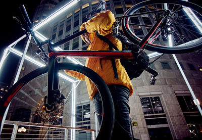 Low angle view of man with bicycle standing against illuminated building at night