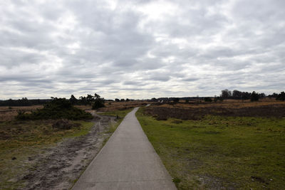 Empty road amidst field against sky