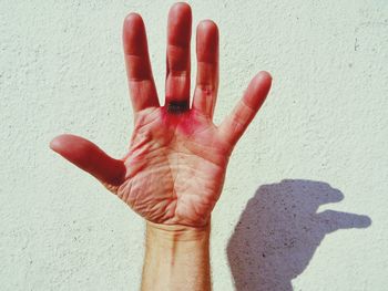 Cropped hand of person against wall during sunny day