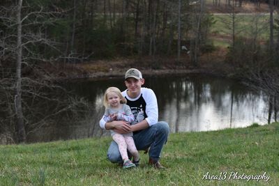 Father and daughter sitting on grass by water