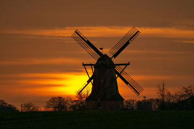 Traditional windmill on field against sky during sunset