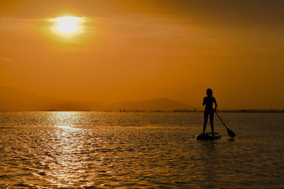 Silhouette woman paddle boarding on sea against sky during sunset