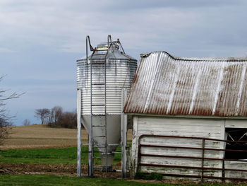 Abandoned water tank by barn against sky