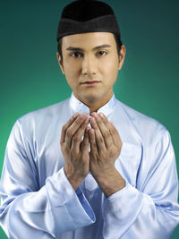 Close-up portrait of man praying against green background