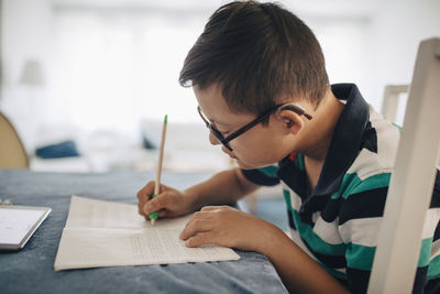 Side view of boy writing on book while sitting at table