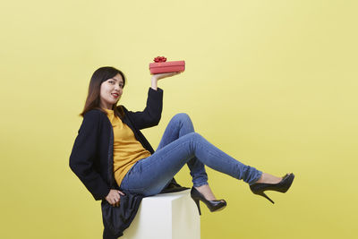 Young woman standing against yellow background