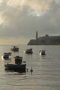 Boats moored in sea against sky during sunset