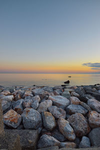 Rocks at sea shore against sky during sunset