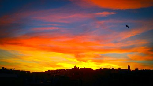 Silhouette of city against orange sky