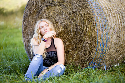 Young woman sitting against hay bales in grass