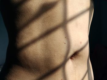 Midsection of shirtless woman in sunlight