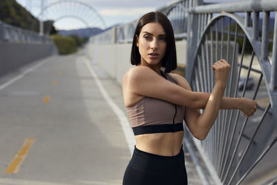 Jogger looking away while stretching arms on bridge