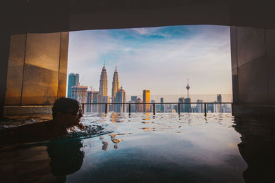 Man swimming in infinity pool against buildings