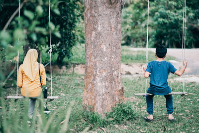 Rear view of boy standing by tree trunk
