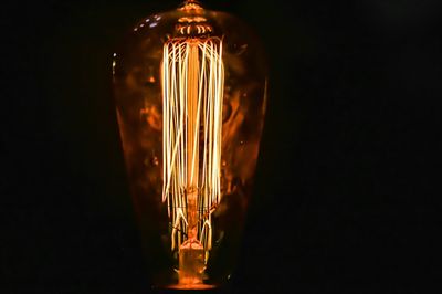 Close-up of illuminated light bulb against black background