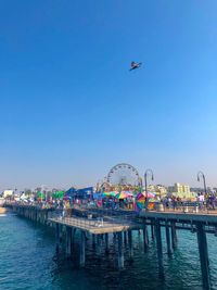 Ferris wheel by pier against clear blue sky