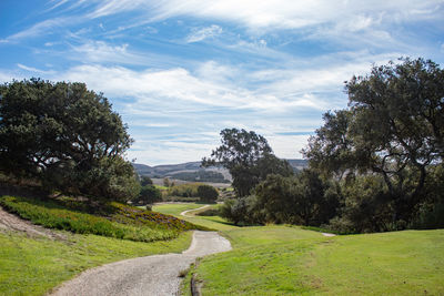 Path amidst trees on golf course against sky