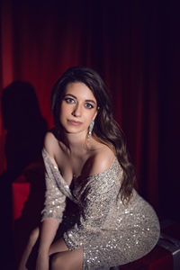 Beautiful young woman in a shiny dress is sitting on red gift boxes with bows in a spot of light