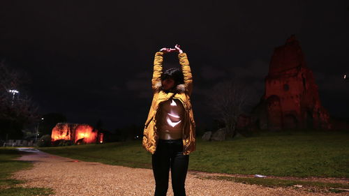 Rear view of man standing on illuminated field against sky at night