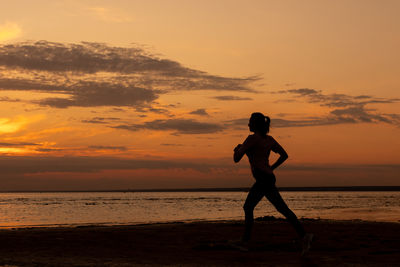 Silhouette woman standing at beach against sky during sunset