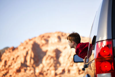 Cheerful boy peeking through car window against sky