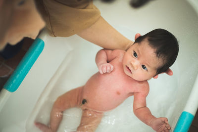 Cropped hand of mother holding naked newborn daughter in bathtub