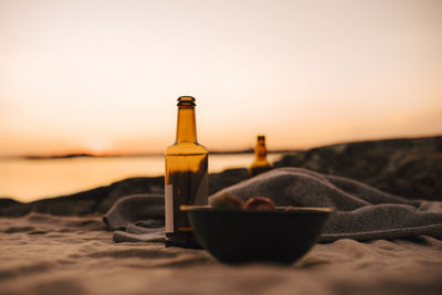 Food bowl and beer bottle at lakeshore during sunset