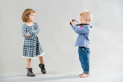 Little boy photographing a girl on a gray background