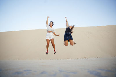 Woman with arms raised on beach against clear sky