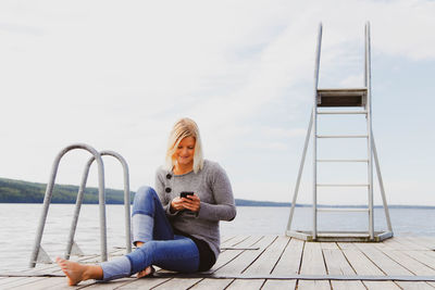 Woman sitting on pier against sky