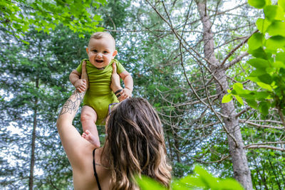 Portrait of happy woman holding plant against trees