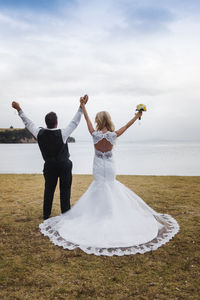 Newlywed couple standing with arms raised at lakeside
