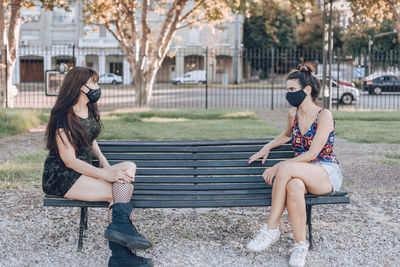 Full length of women wearing mask sitting on bench in park