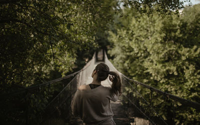 Rear view of woman standing on footbridge in forest