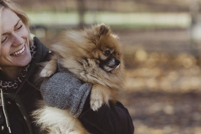 Smiling woman embracing fluffy pomeranian dog at park