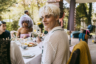 Portrait of smiling gay man with gray hair sitting amidst friends during dinner party in back yard