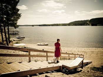 Rear view of woman sitting on pier against lake