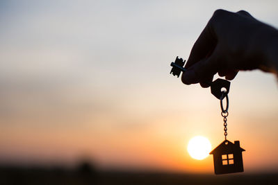 Silhouette of a house figure with a key, a pen with a keychain on the background of the sunset. 