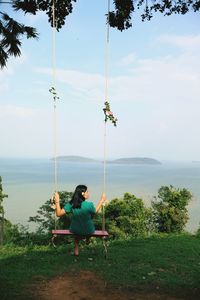 Man sitting on swing in sea against sky