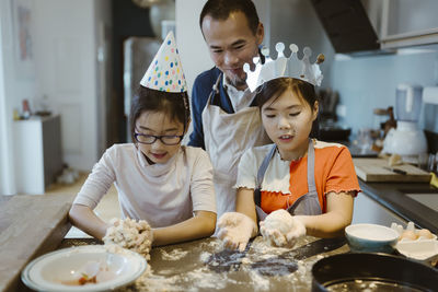 Father watching daughters kneading dough in kitchen at home