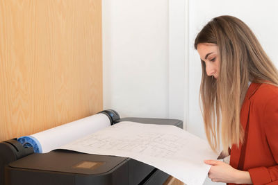 Young woman in architecture office printing blueprints in plotter