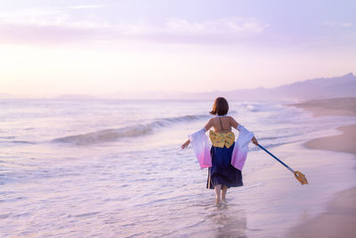 Rear view of woman on beach against sky during sunset