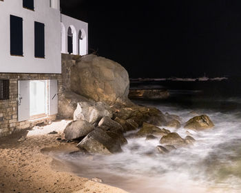 Rocks on beach by buildings against sky