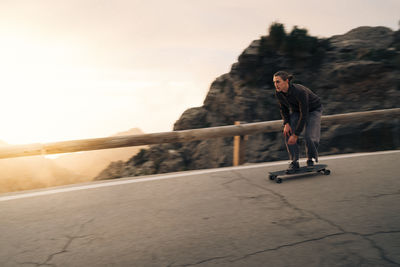 Man skateboarding near railing on road at sunset