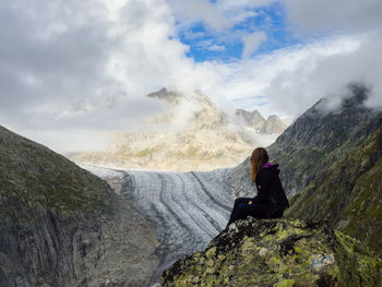 Woman sitting on rock against cloudy sky