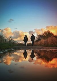 Silhouette people standing by lake against sky during sunset