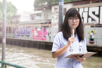 Thoughtful female doctor holding book while standing outdoors