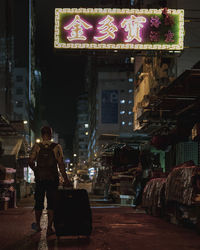 Rear view of man walking on illuminated street at night