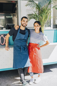 Full length portrait of smiling young colleagues standing against food truck